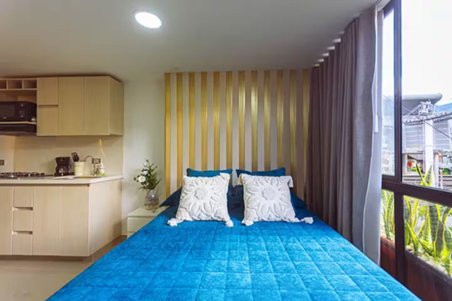 Une chambre avec un lit, une fenêtre avec des rideaux, un coin cuisine et une vue sur l’extérieur.
