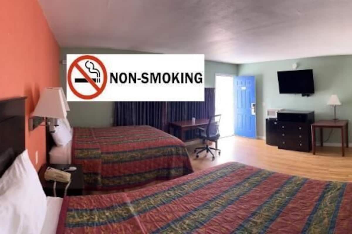 A non-smoking hotel room with two beds, a desk, a chair, a television, and a mirror.