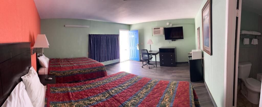 A hotel room with two beds, a desk, a chair, a television, and a bathroom.