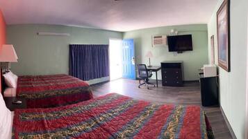 A hotel room with two beds, a desk, a chair, a television, and a bathroom.