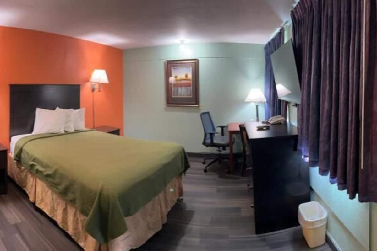 A hotel room with a bed, desk, chair, and a small kitchenette.