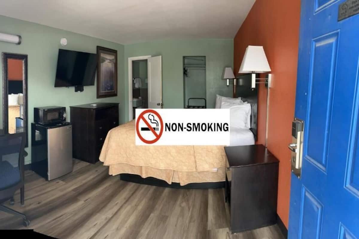 A hotel room with a bed, desk, chair, television, and a non-smoking sign.