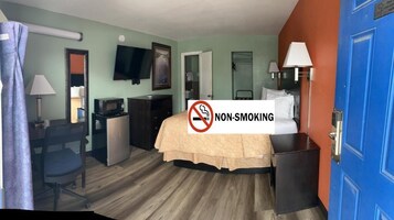 A hotel room with a bed, desk, chair, television, and a non-smoking sign.