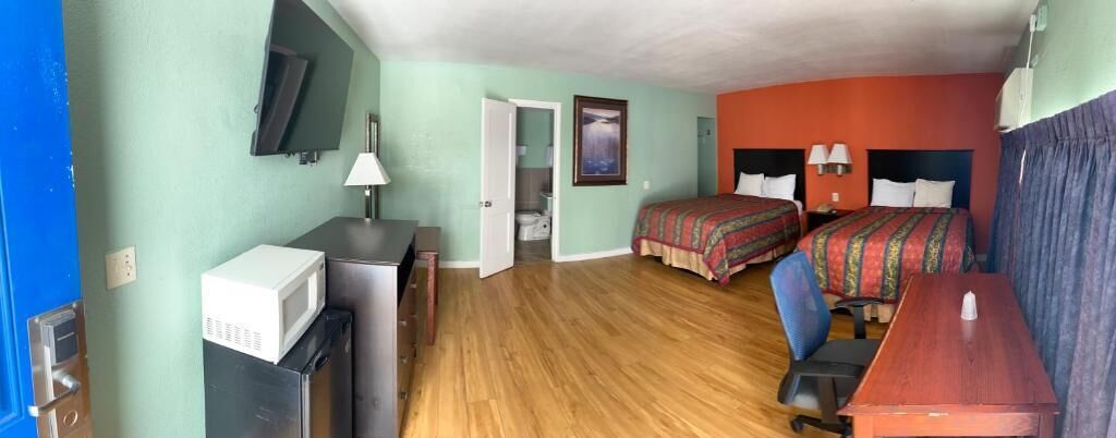 A room with two beds, a desk, a microwave, a TV, and a door leading to a bathroom.