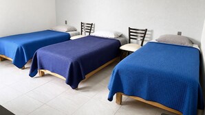 Una habitación con tres camas individuales, cada una con colcha azul, cabeceros de madera y paredes blancas.