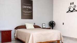 Un dormitorio con cama, mesita de noche, ventilador de pared y un póster motivacional.