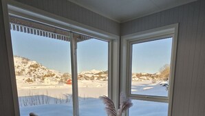 Una stanza con due sedie nere, un tavolino rotondo e un vaso con fiori secchi. Grandi finestre offrono vista su un paesaggio innevato.