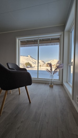 Ein Zimmer mit einem großen Fenster, einem Sessel und einer Vase mit Trockenblumen.
