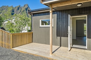 Um deck de madeira com porta que dá para um quarto, uma janela e vista para montanhas.