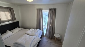 Habitació d'hotel amb llit, cortines, una taula petita i finestra amb vista.