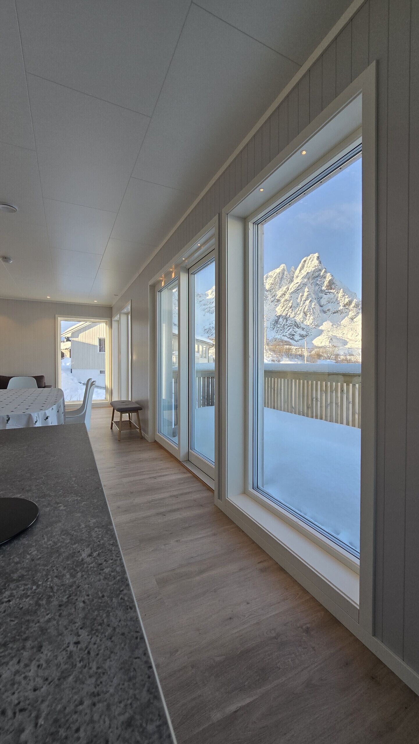 A modern interior with large windows, a wooden floor, and a view of snow-covered mountains.