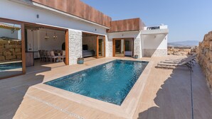 A modern outdoor pool area with a stone wall, a dining area, and a view of the landscape.