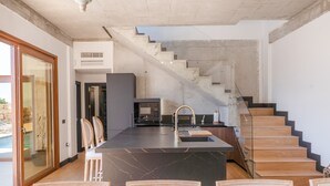 A modern kitchen with a central island, a staircase, and a dining area with chairs.