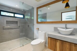 Un baño moderno con cabina de ducha de vidrio, inodoro, tocador con lavamanos y un espejo grande.