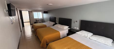 A hotel room with three beds, a desk, and a television.