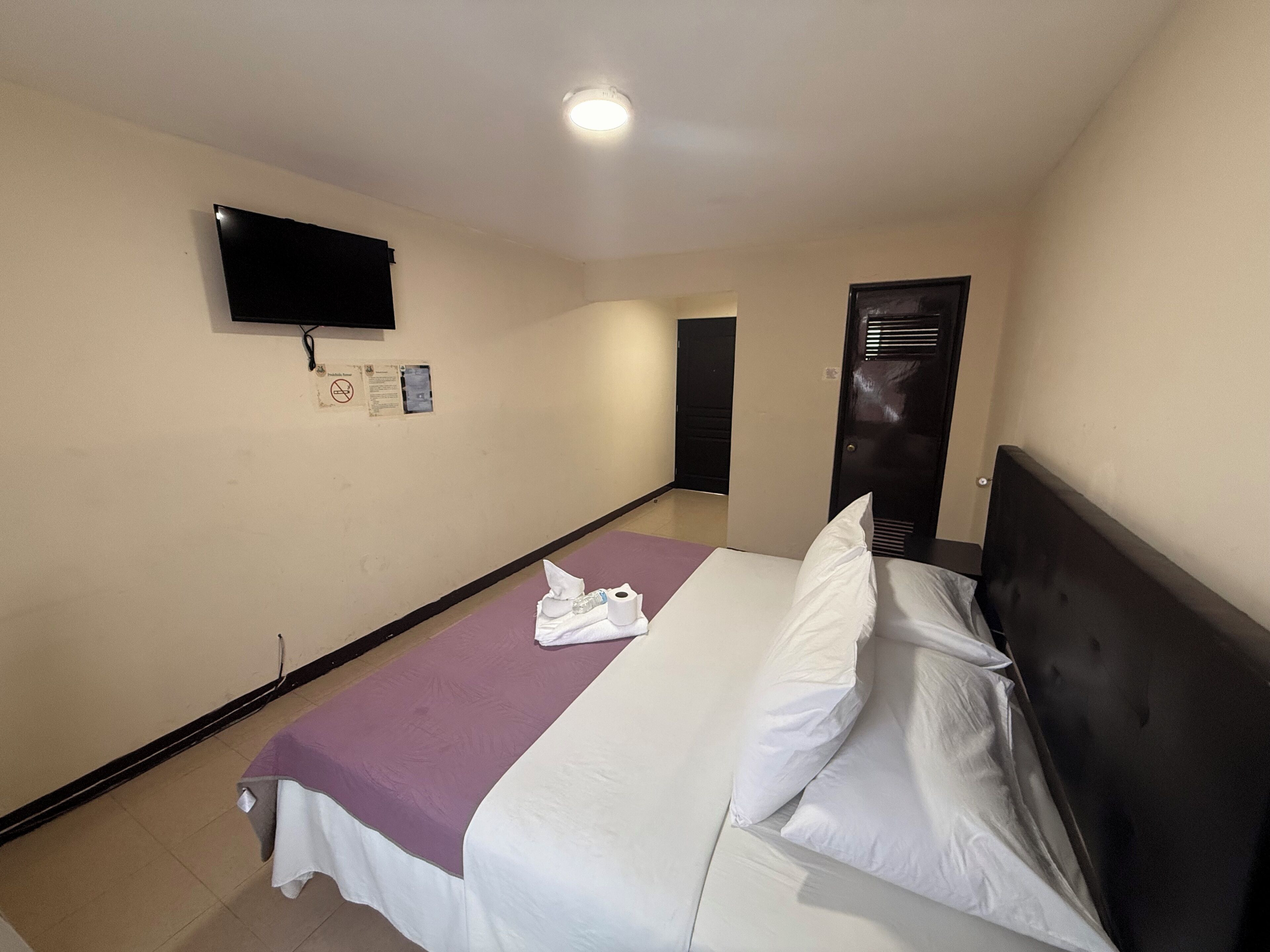 Een hotelkamer met een bed, een aan de muur bevestigde televisie en een deur naar een andere kamer.