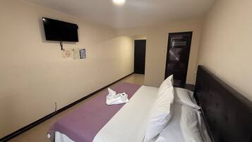 Een hotelkamer met een bed, een aan de muur bevestigde televisie en een deur naar een andere kamer.