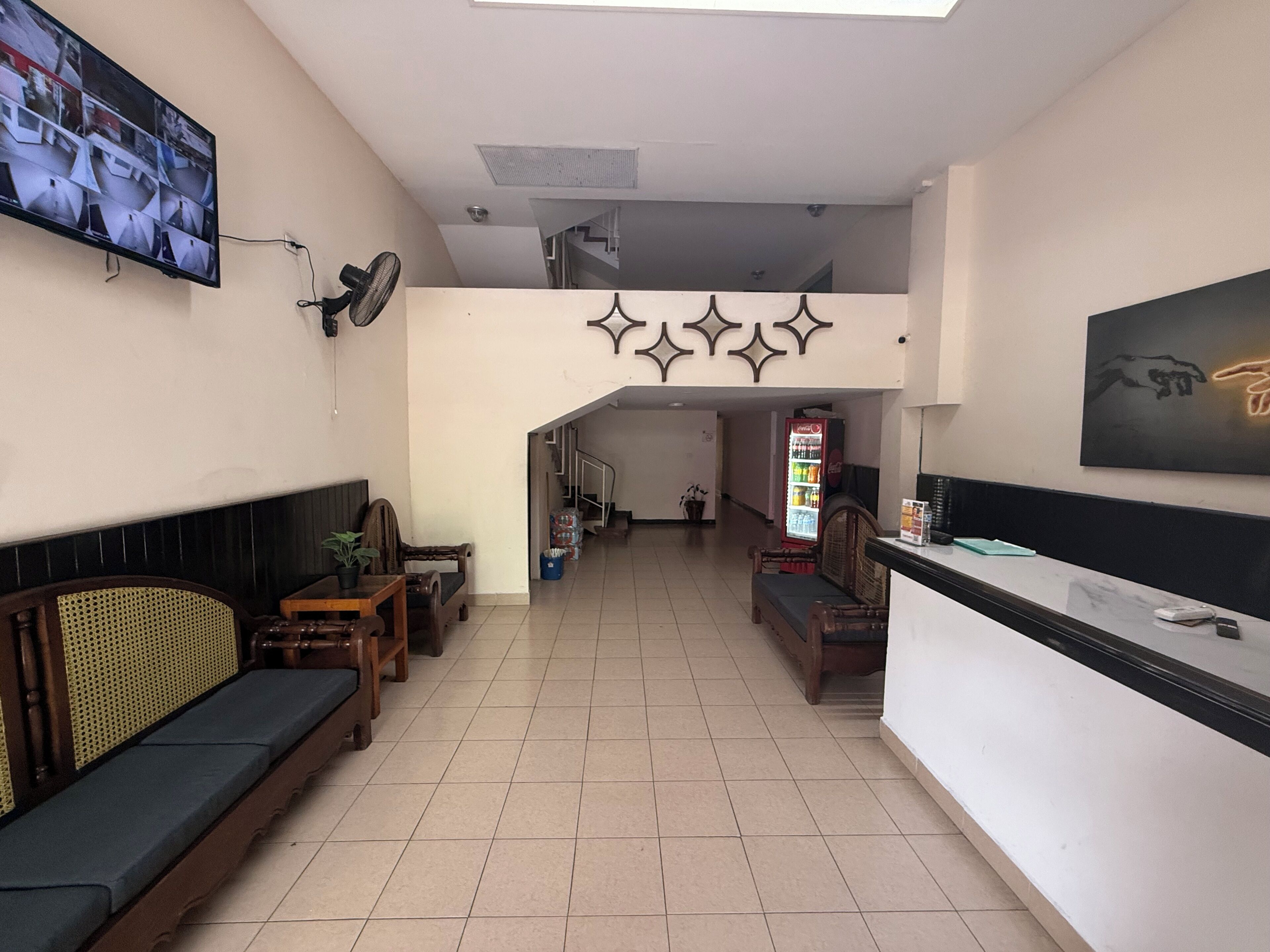 Un área de recepción con un sofá, sillas, un televisor, un refrigerador de Coca-Cola y una escalera.