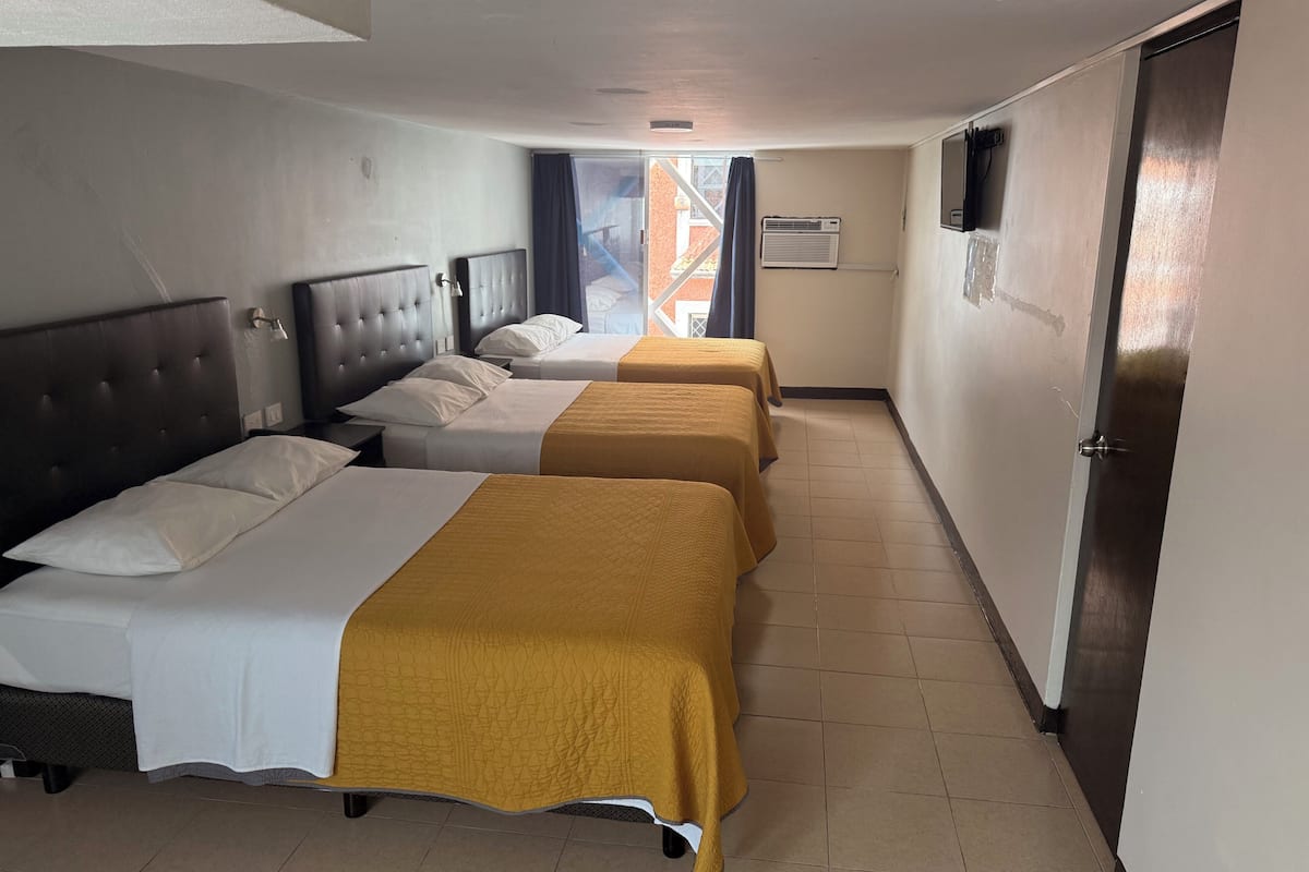 Ein Hotelzimmer mit drei Betten, einem Fernseher und einem Fenster mit Vorhängen.