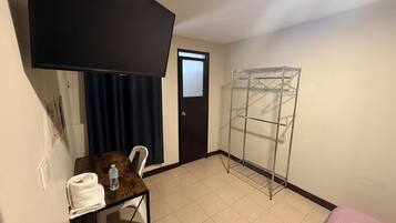 A room with a TV mounted on the wall, a metal drying rack, a small table with a towel and water bottle, and a door with a window.