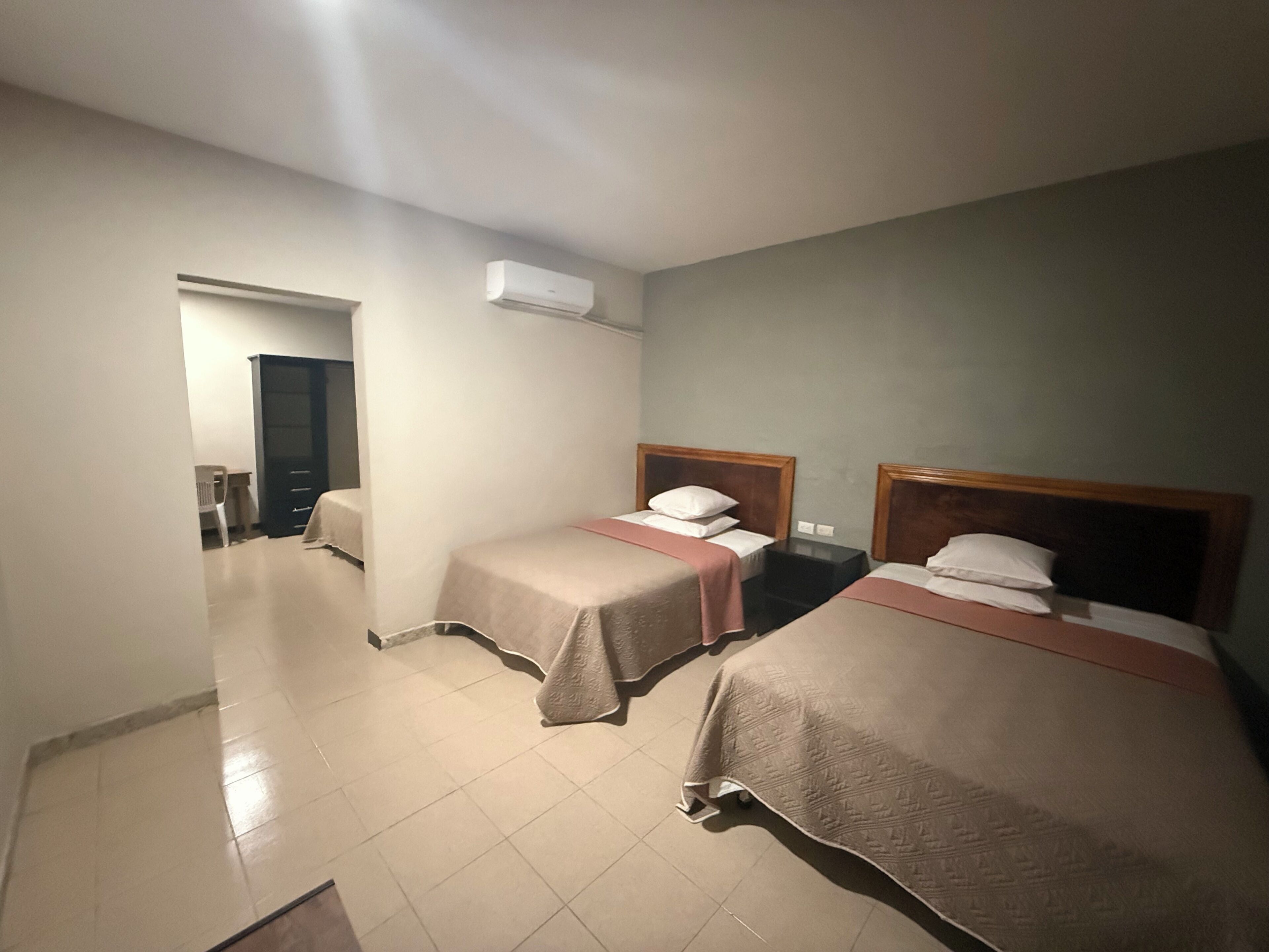 Una camera d'albergo con tre letti, una scrivania e un condizionatore d'aria.