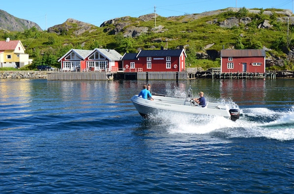A boat speeding across calm water with a row of red buildings in the background.