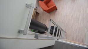 Ein modernes Interieur mit weißer Wand, Metallgeländer, einem schwarzen zylindrischen Gegenstand und einem roten Sessel.