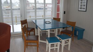 Ein Essbereich mit Tisch und Stühlen, große Fenster mit Blick auf verschneite Landschaft, und ein gerahmtes Bild an der Wand.