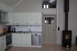 A modern kitchen with white cabinetry, a dishwasher, a stove, and a black wood-burning stove. - Thor-Bua, Sund in Lofoten (Flakstad)