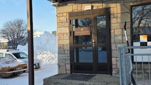 Ingresso di un edificio con facciata in pietra, ringhiera metallica e terreno innevato.