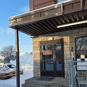 A building entrance with a stone facade, a metal railing, and a snow-covered ground.
