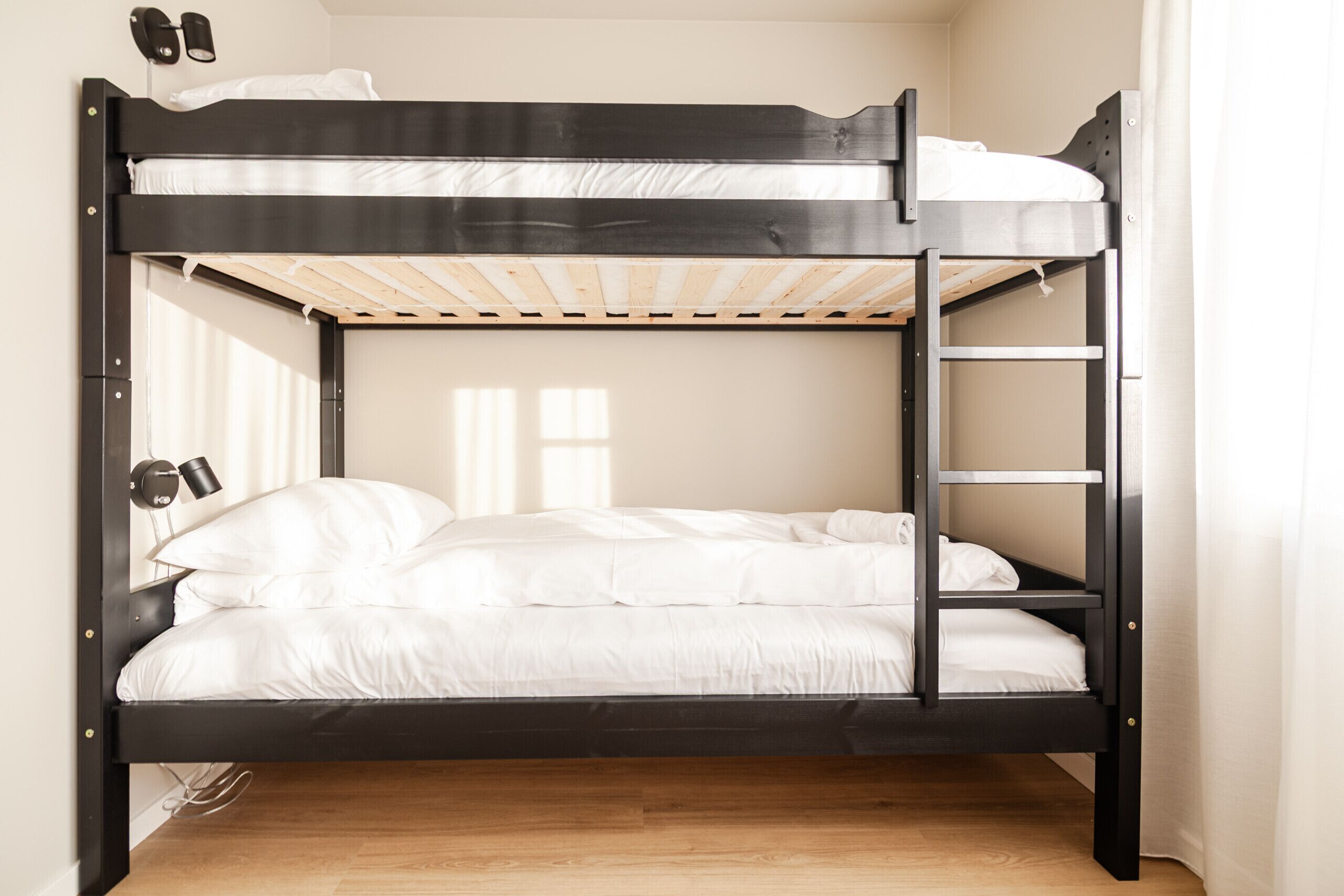 A bunk bed with a wooden ladder, white bedding, and a desk lamp.