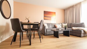 Un soggiorno moderno con zona pranzo, un divano grigio, un tavolino da caffè e un quadro raffigurante un tramonto sulla parete.
