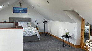 A bedroom with a sloped ceiling, a bed with floral bedding, a nightstand, a desk, a hanging coat rack, and a painting of a landscape. - Studio Sleeps 2 -private Hot Tub -enclosed Garden (Killarney)