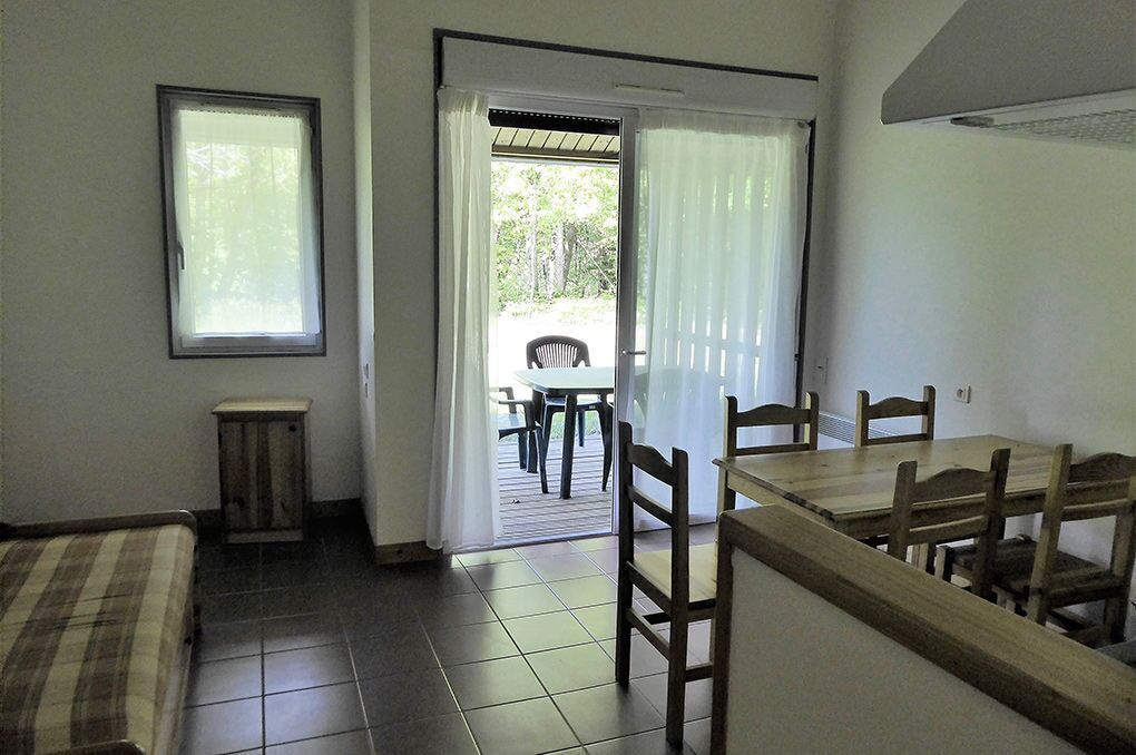 Una habitación con cama, un pequeño armario, una mesa de comedor con sillas, una ventana y una puerta que da a un espacio al aire libre.