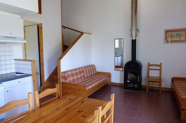 Un espacio habitable compacto con kitchenette, sofá, mesa de comedor, chimenea y escalera.