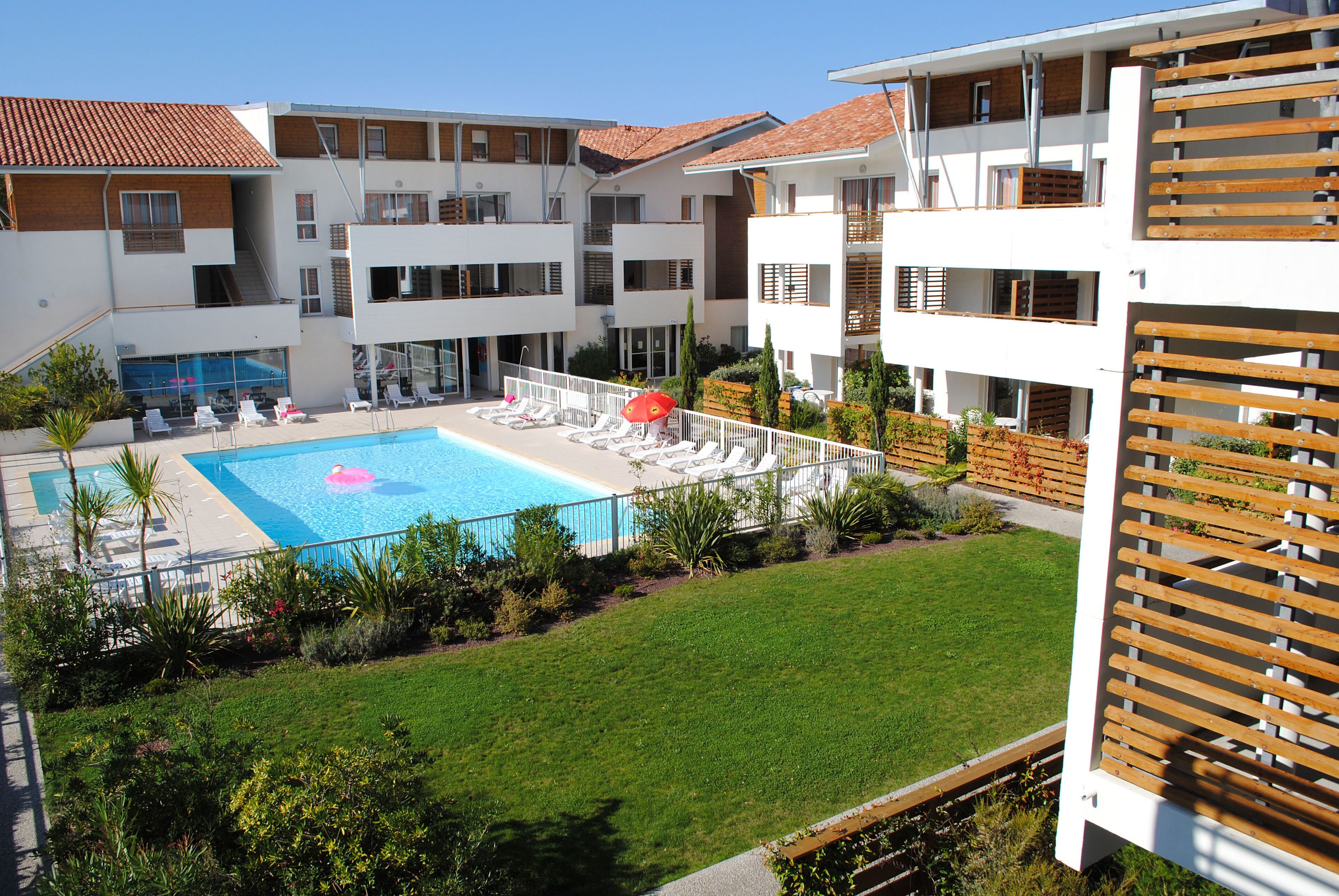 A hotel with a swimming pool, lounge chairs, and a well-maintained lawn.