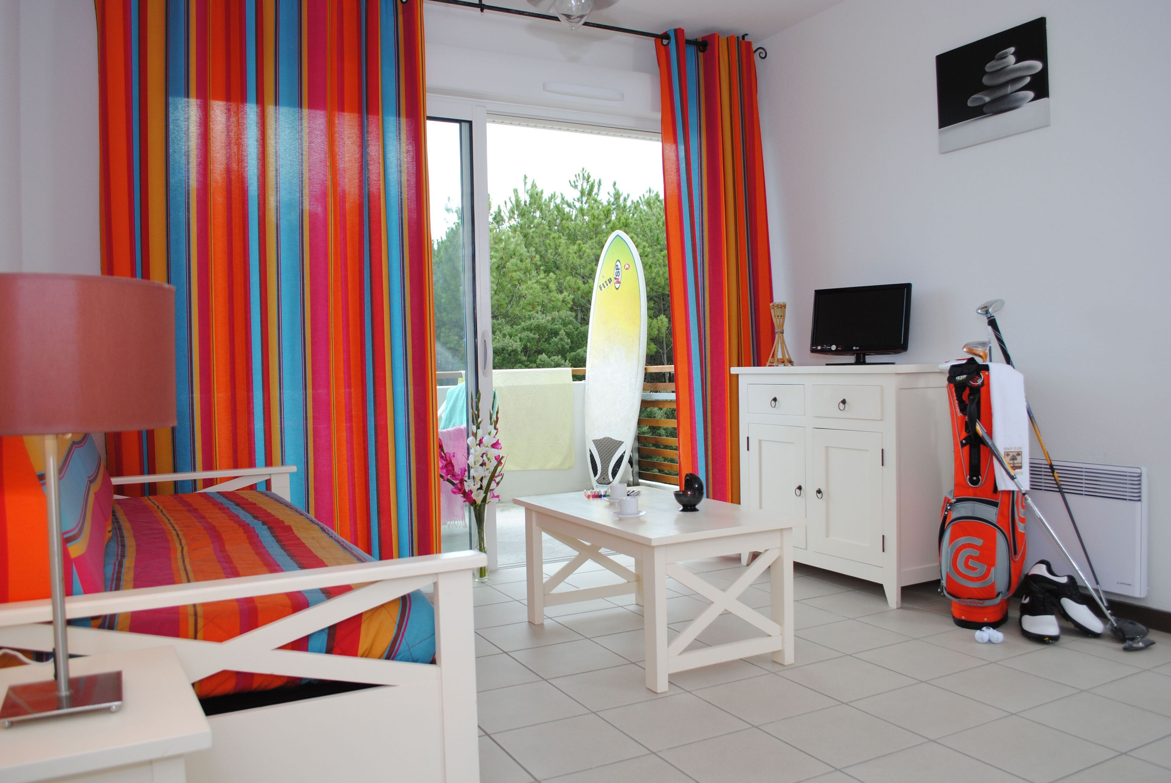 Une pièce comprenant un lit, une table, un téléviseur, une planche de surf et un sac de golf.