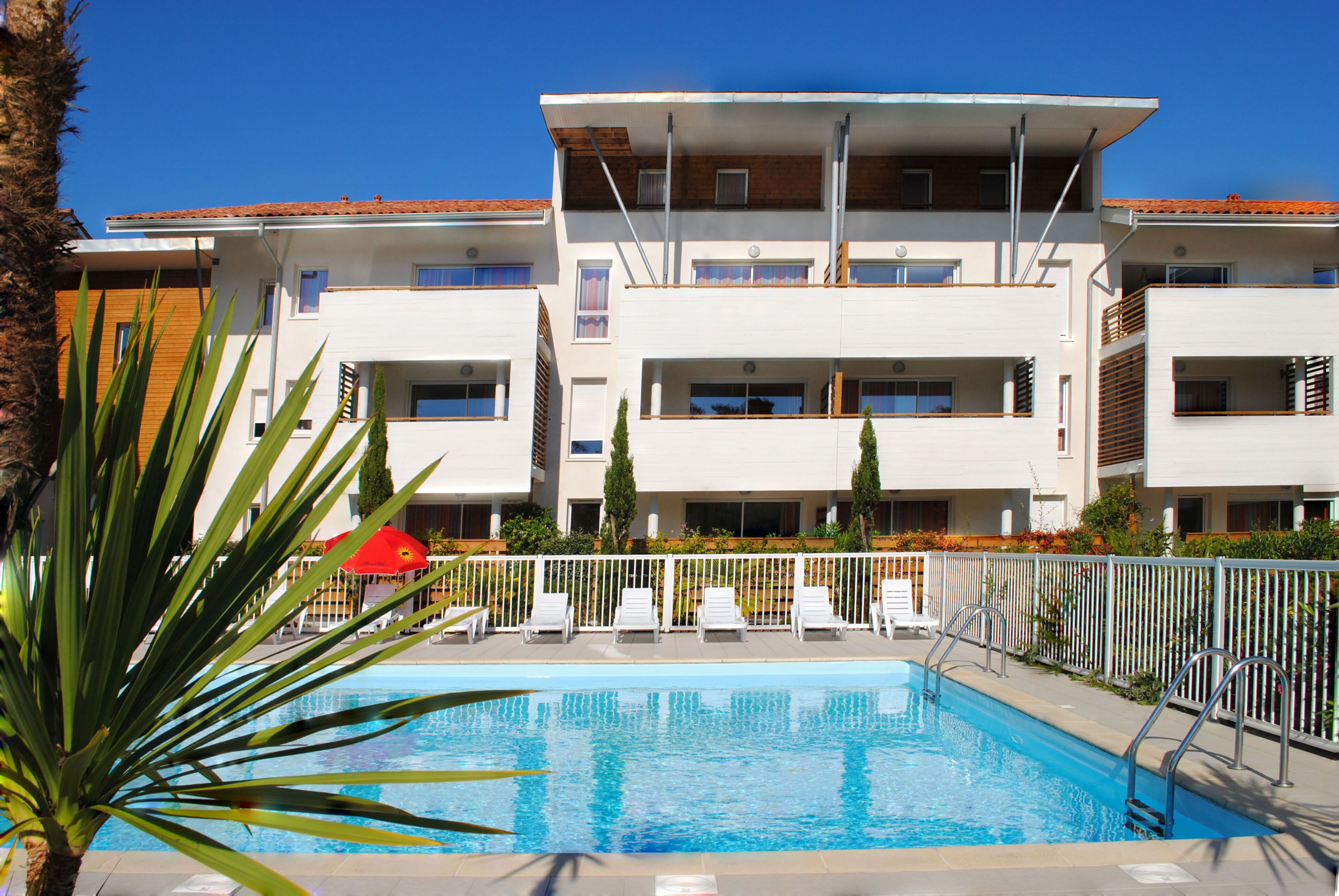 A swimming pool with lounge chairs and a building with balconies in the background.