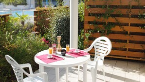 A round white table with two white chairs, pink placemats, and a glass of orange juice. - À 200 m de la plage et du golf | Piscines | Sauna (Moliets)