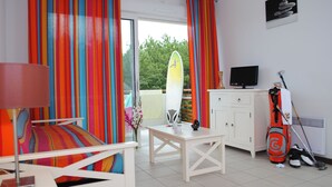A room with a bed, a table, a television, a surfboard, and a golf bag. - À 200 m de la plage et du golf | Piscines | Sauna (Moliets)