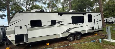 A white RV with the brand name 'COUGAR' on the side, equipped with a sliding door, a small window, and a mounted air conditioning unit.