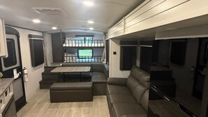 Interior compacto de una caravana con cocina, zona de estar y televisor.