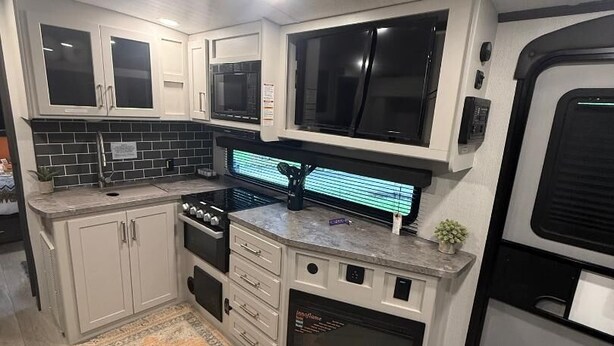 Una cocina compacta con armarios blancos, un microondas, una estufa y una pequeña alfombra en el suelo.