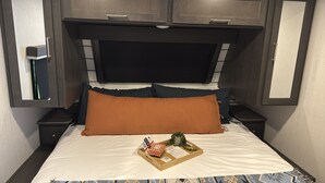 Una cama con colchón blanco, dos almohadas, una bandeja con una planta pequeña y un menú.