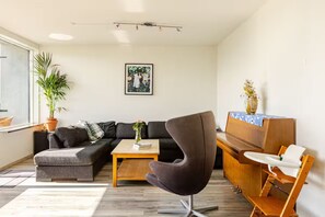 Un salon moderne avec un canapé d’angle, un fauteuil foncé, une table basse en bois et une petite table d’appoint sur laquelle est posé un vase.