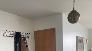 A room with a wooden door, a coat rack with jackets, a hanging light fixture, a small table, and a patterned rug.