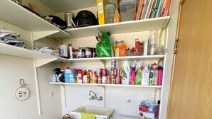 A compact laundry room with a washing machine, shelves with various items, a sink, and a wicker basket.