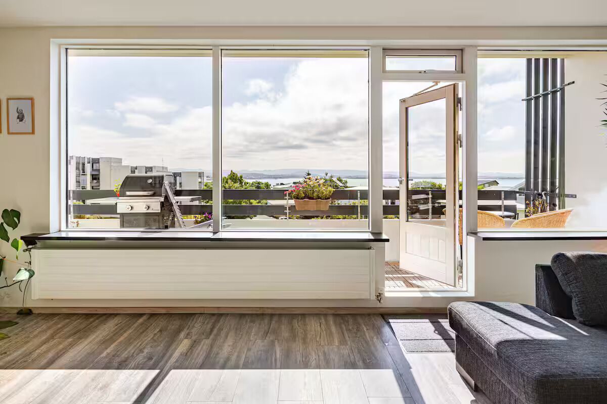 A modern living room with a large sliding glass door leading to a balcony with a view of the cityscape.