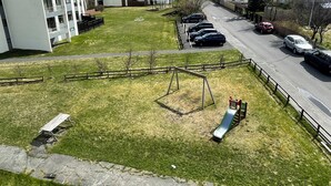 A residential area with a playground, parked cars, and a building with balconies.
